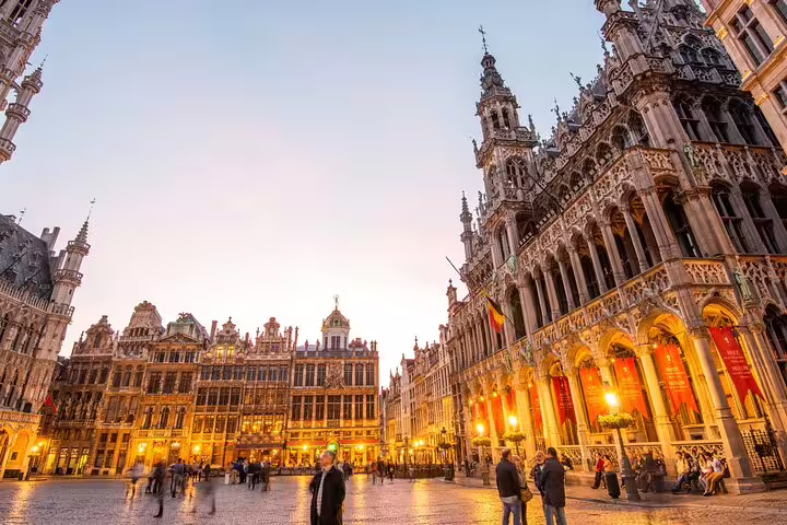 Grand Place Brussels at dusk with illuminated Gothic buildings and tourists on cobblestone square