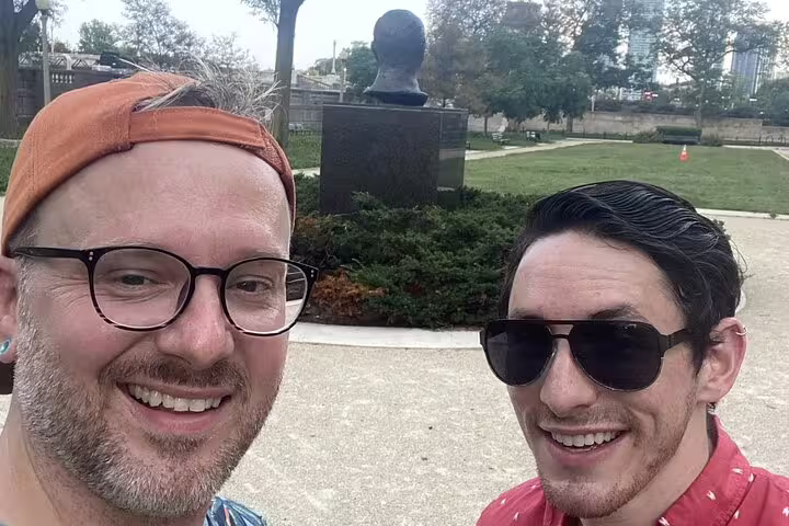 Two smiling men taking a selfie in Grant Park Chicago with a bronze bust sculpture behind them