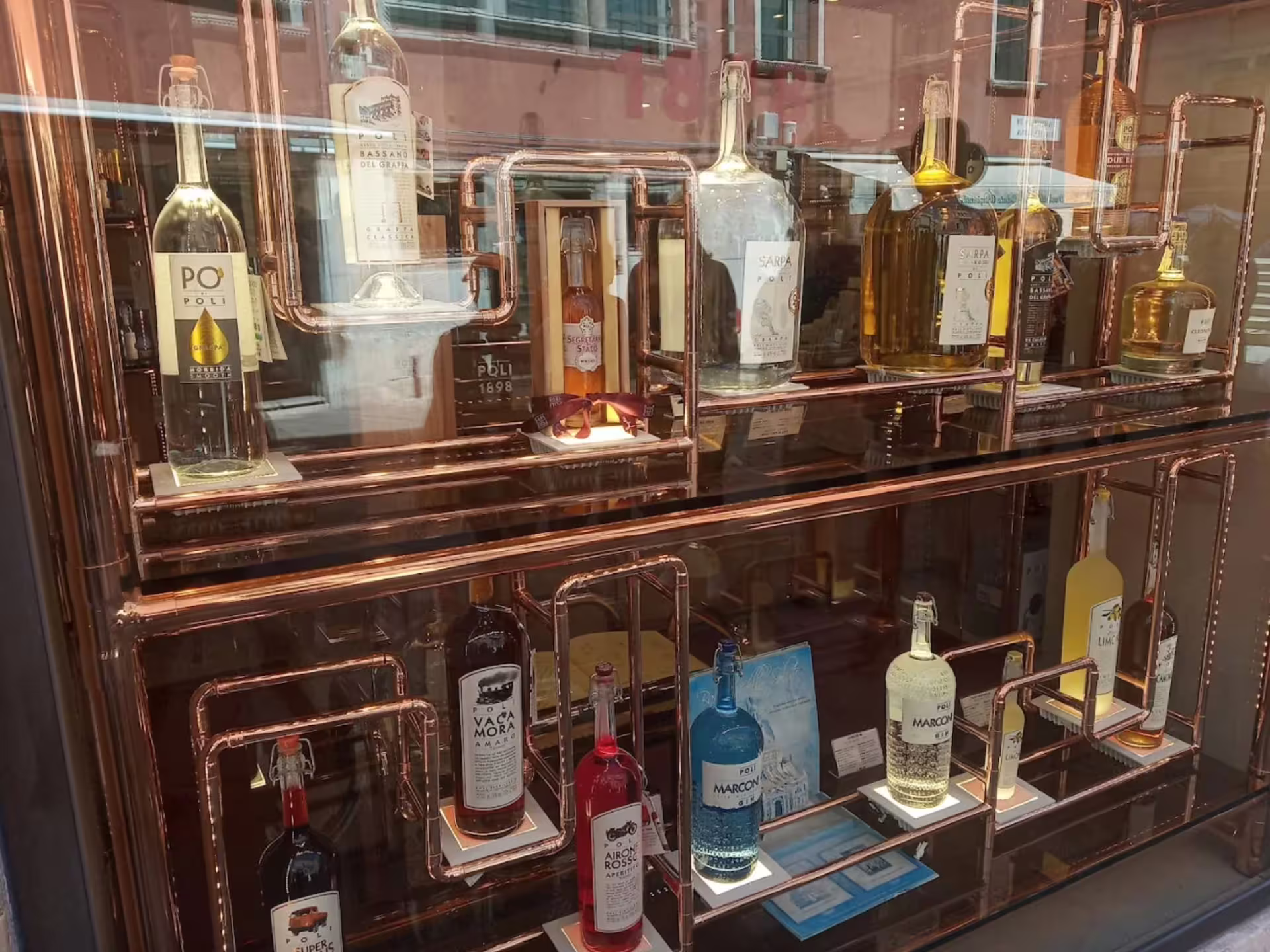 Display of assorted grappa bottles in a Venice shop window, showcasing exclusive flavors for tasting tours.