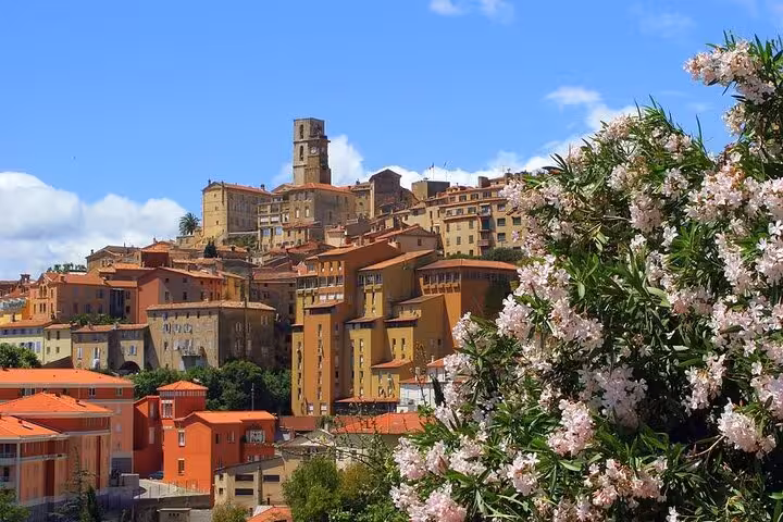 Hilltop village of Grasse with terracotta rooftops, stone clock tower, and pink oleander flowers in foreground