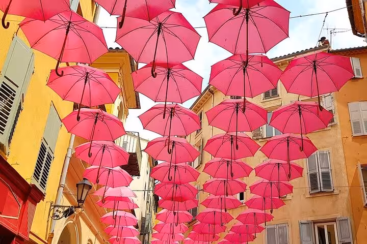 Vibrant pink umbrellas floating above colorful Grasse old town streets on a private Provence perfume village tour