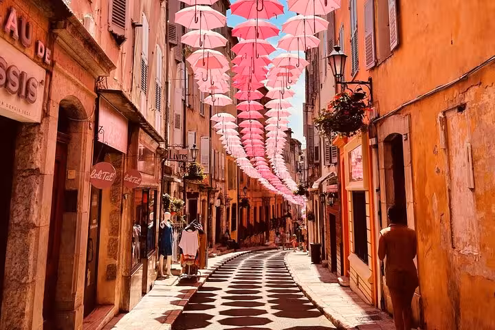 Charming Grasse old town street adorned with pink umbrellas overhead during a private Provence medieval village tour