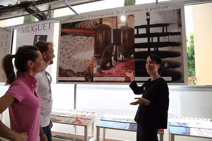 Tour guide presenting perfume extraction methods exhibit in Grasse perfumery museum to two visitors