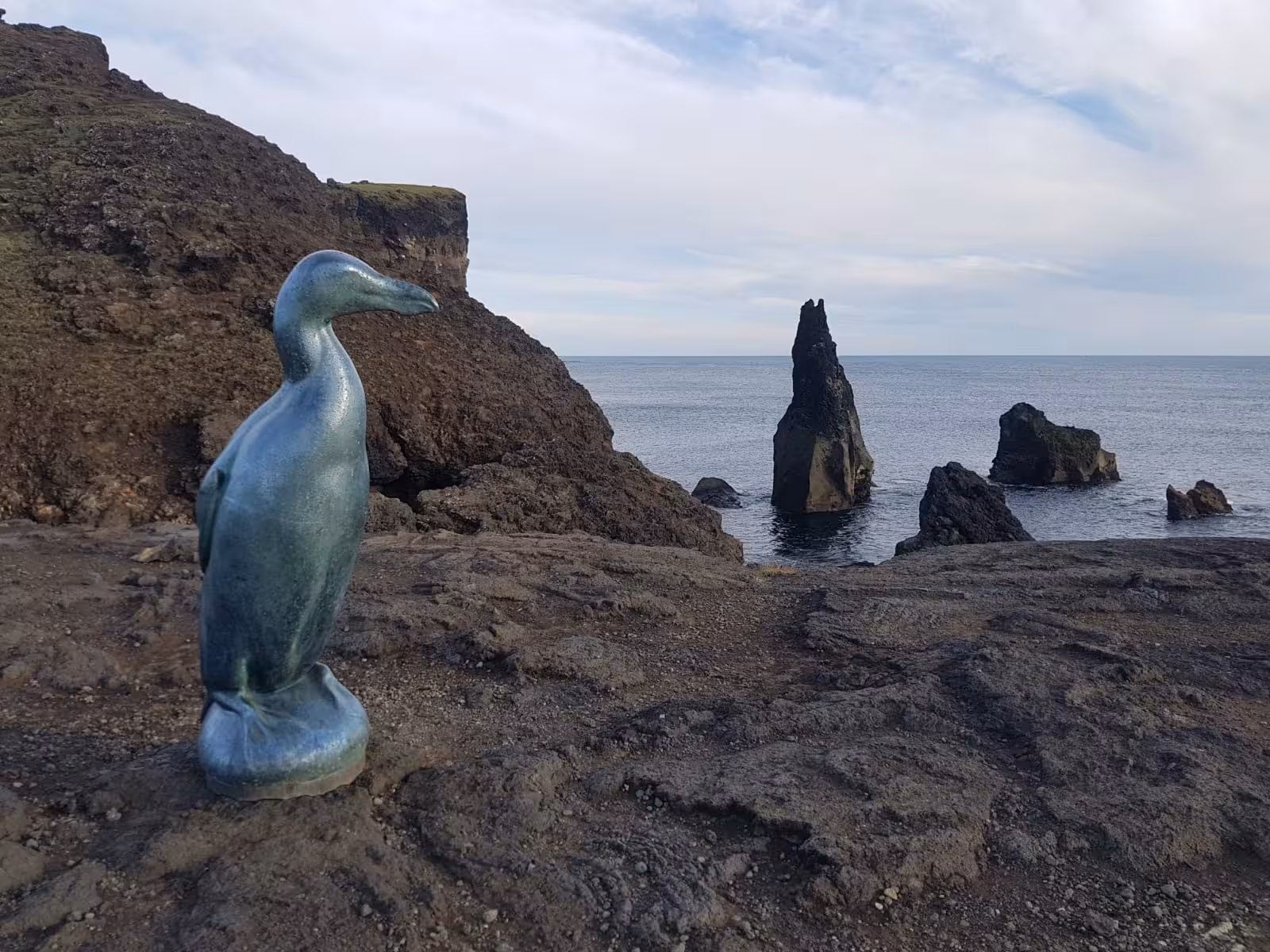 Bronze great auk statue on volcanic rock coast with dramatic sea stacks in Reykjanes Geopark, Iceland