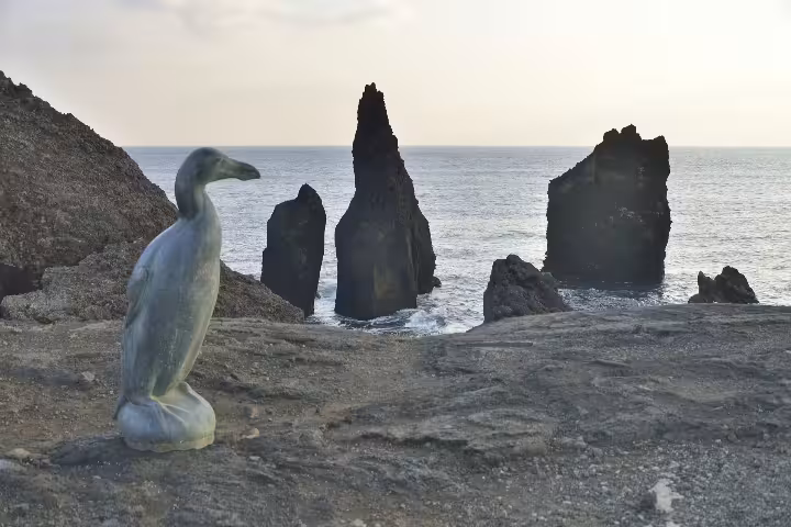 Great Auk statue on rocky coastline with dramatic basalt sea stacks at Reykjanes Peninsula, Iceland