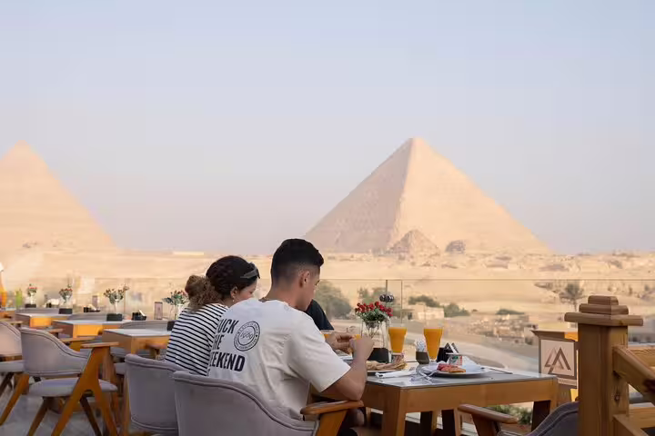 Guests enjoying lunch on Great Pyramid Inn rooftop terrace with panoramic Giza Pyramids view, Cairo