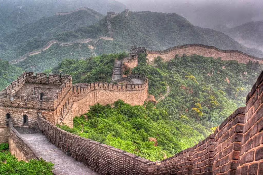 Scenic view of the Great Wall of China winding through lush green mountains, highlighting its historical significance.
