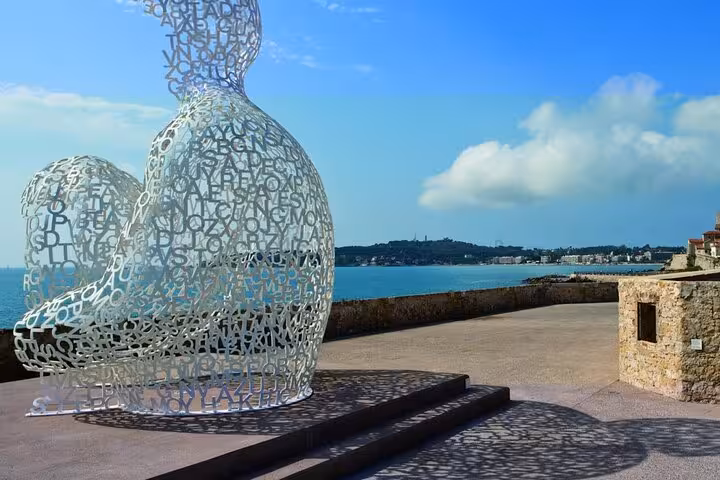 Artistic sculpture of intertwined letters overlooking the serene French Riviera coastline on a sunny day.