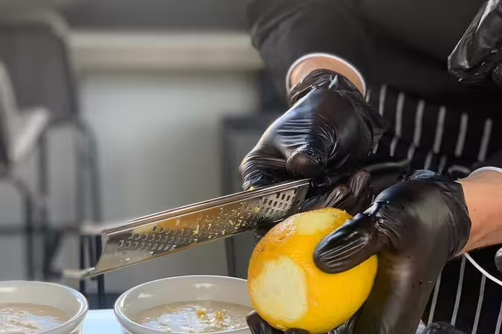 Chef zesting fresh lemon during Greek cooking class in Athens, preparing rooftop dinner with Acropolis view