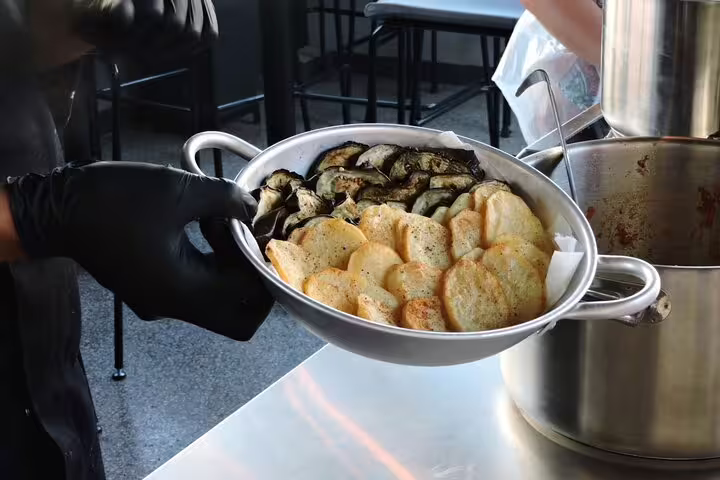 Gloved hands serving fried zucchini and potatoes in Athens Greek cooking class before rooftop dinner with views