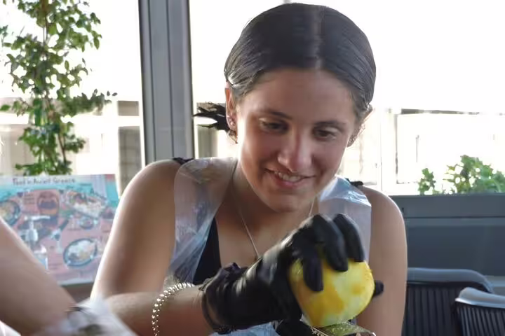 Guest zesting lemon during Greek cooking class in Athens, preparing authentic recipes before rooftop dinner with Acropolis view