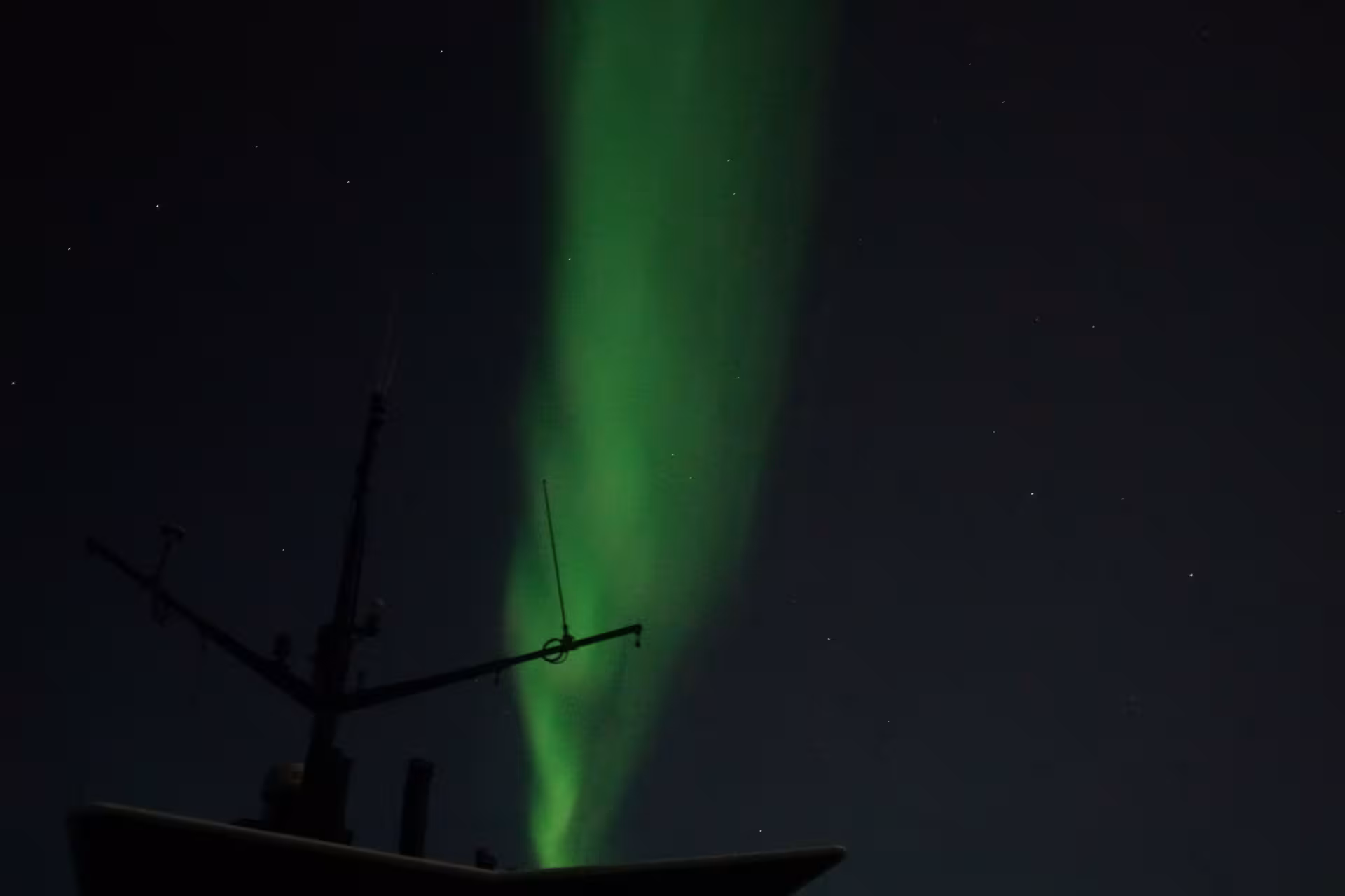 Green Aurora Borealis illuminating the dark ocean near Reykjavík