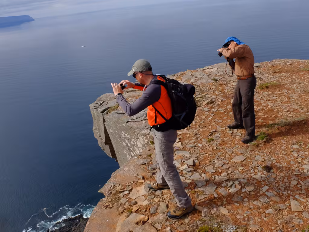 Hikers photographing dramatic Hornstrandir coastal cliffs above the Arctic Ocean on a Westfjords tour