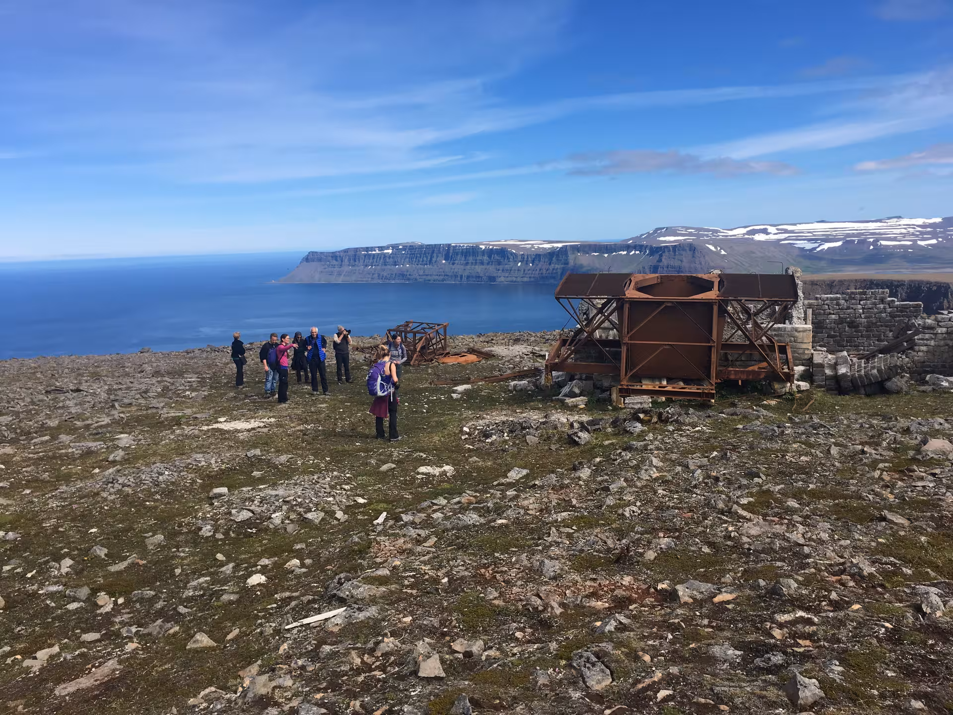 Hikers explore Hornstrandir’s green sea cliffs by rusted ruins, overlooking Ísafjarðardjúp fjord in Iceland