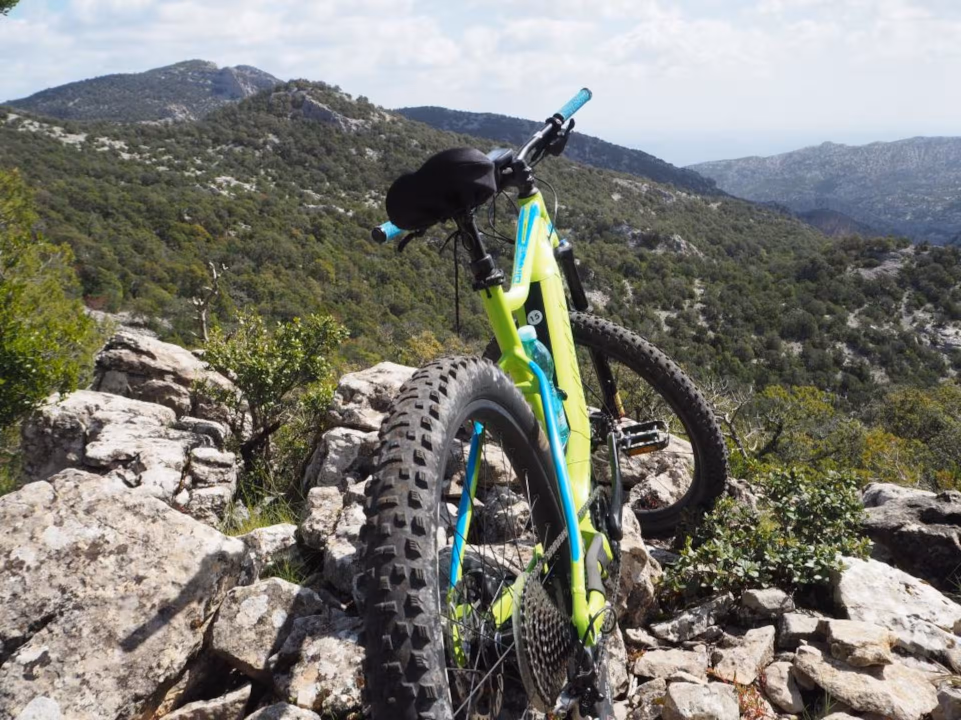 Bright green e-bike parked on rocky terrain overlooking lush Sardinian hills near Olbia.