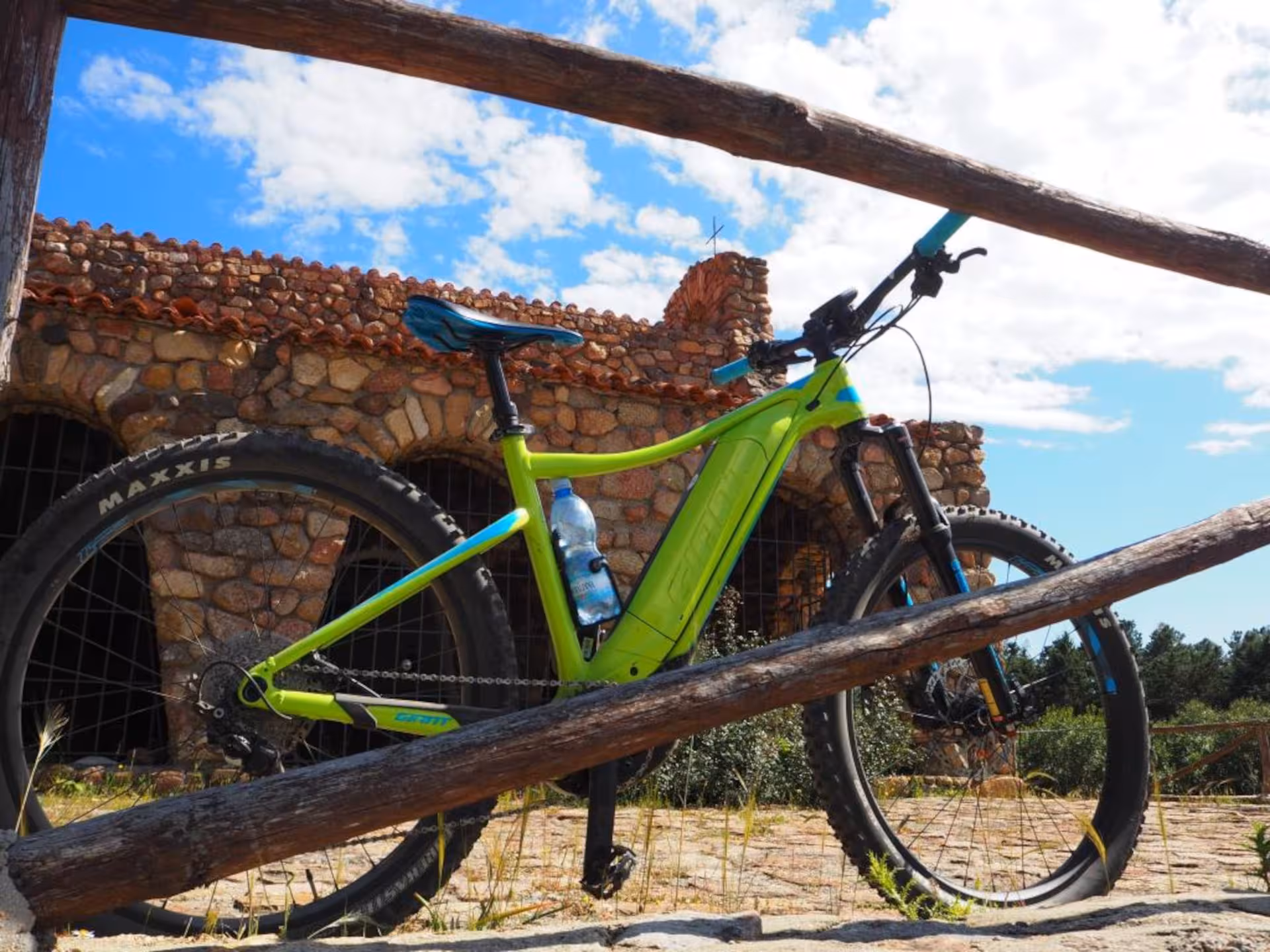 Green e-bike parked near a rustic stone building under a bright Sardinian sky.