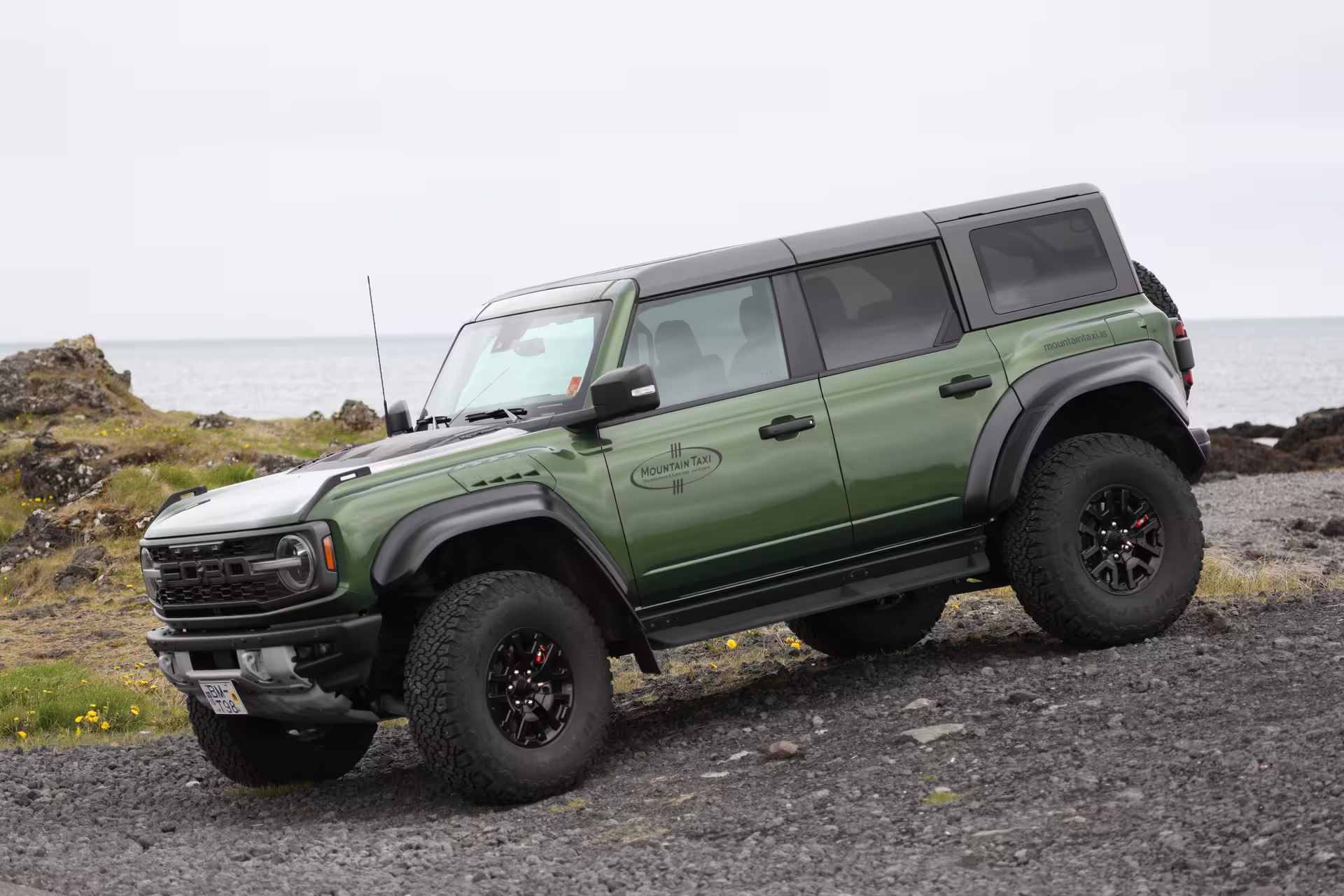 Green Ford Bronco Raptor super jeep parked on rocky volcanic terrain near the ocean in Iceland