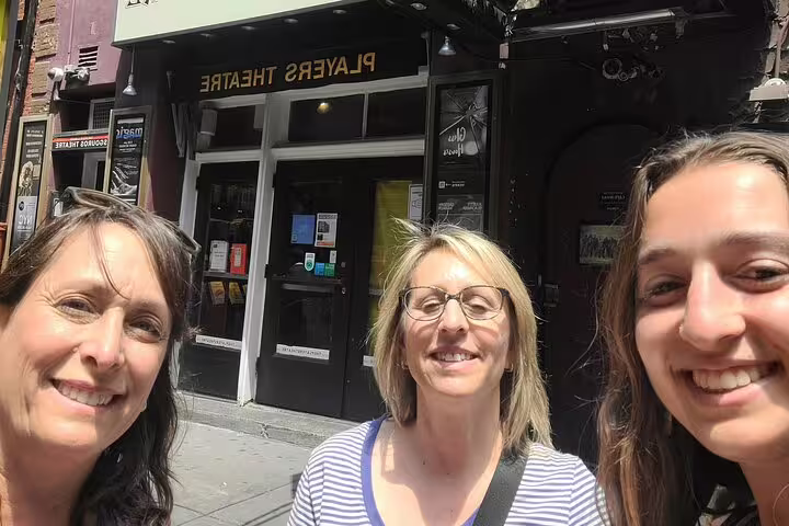 Three women smiling outside Players Theatre in Greenwich Village on a sunny day