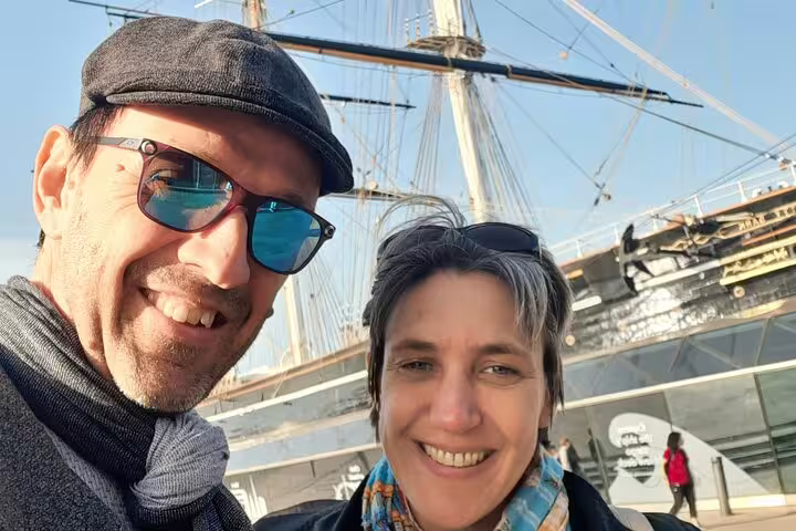 Couple smiling in selfie with tall ship masts at Greenwich waterfront on walking tour