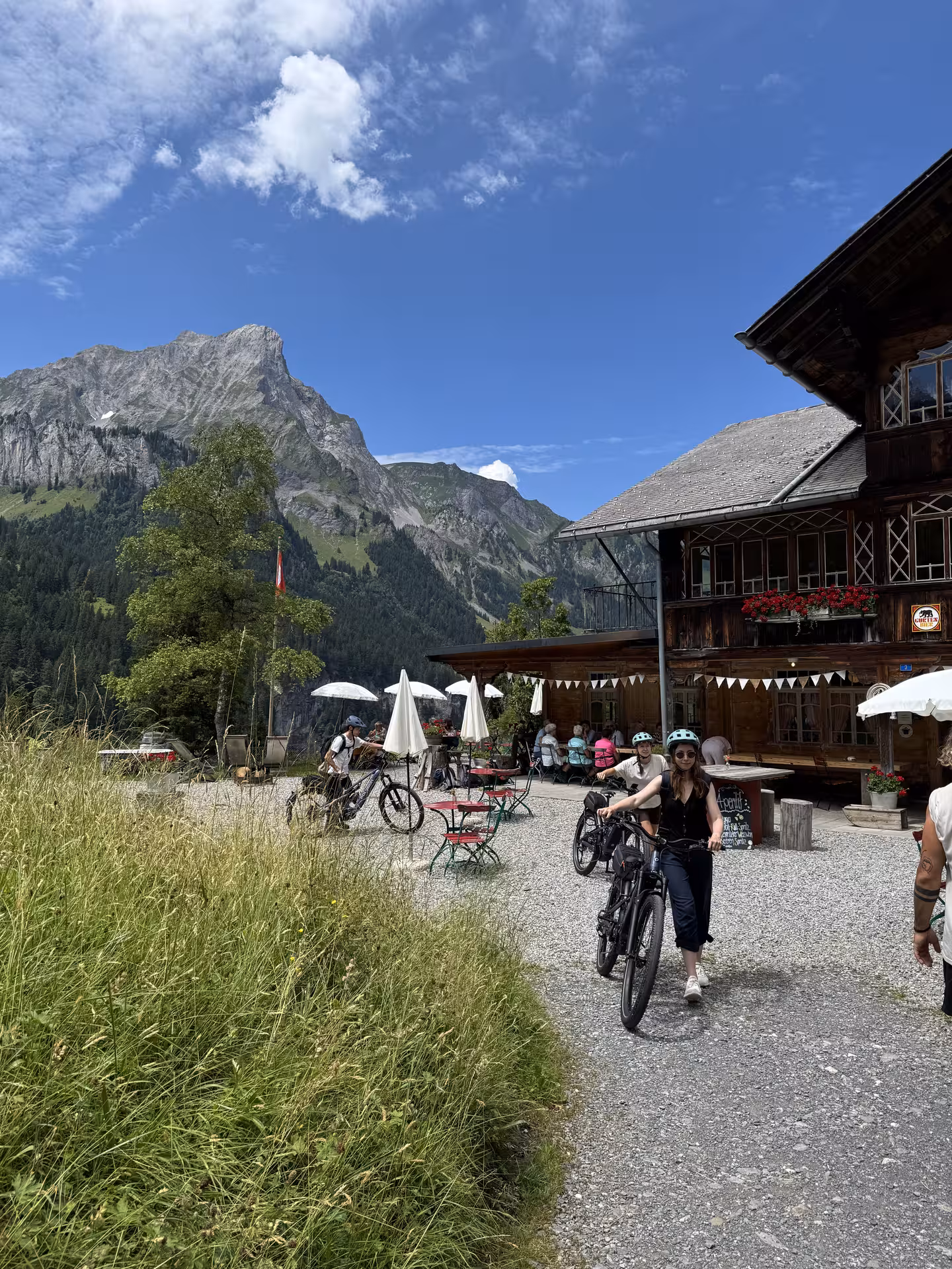 E-bike riders at a rustic mountain chalet in Griesalp UNESCO alpine valley, Swiss Alps tour with peaks view