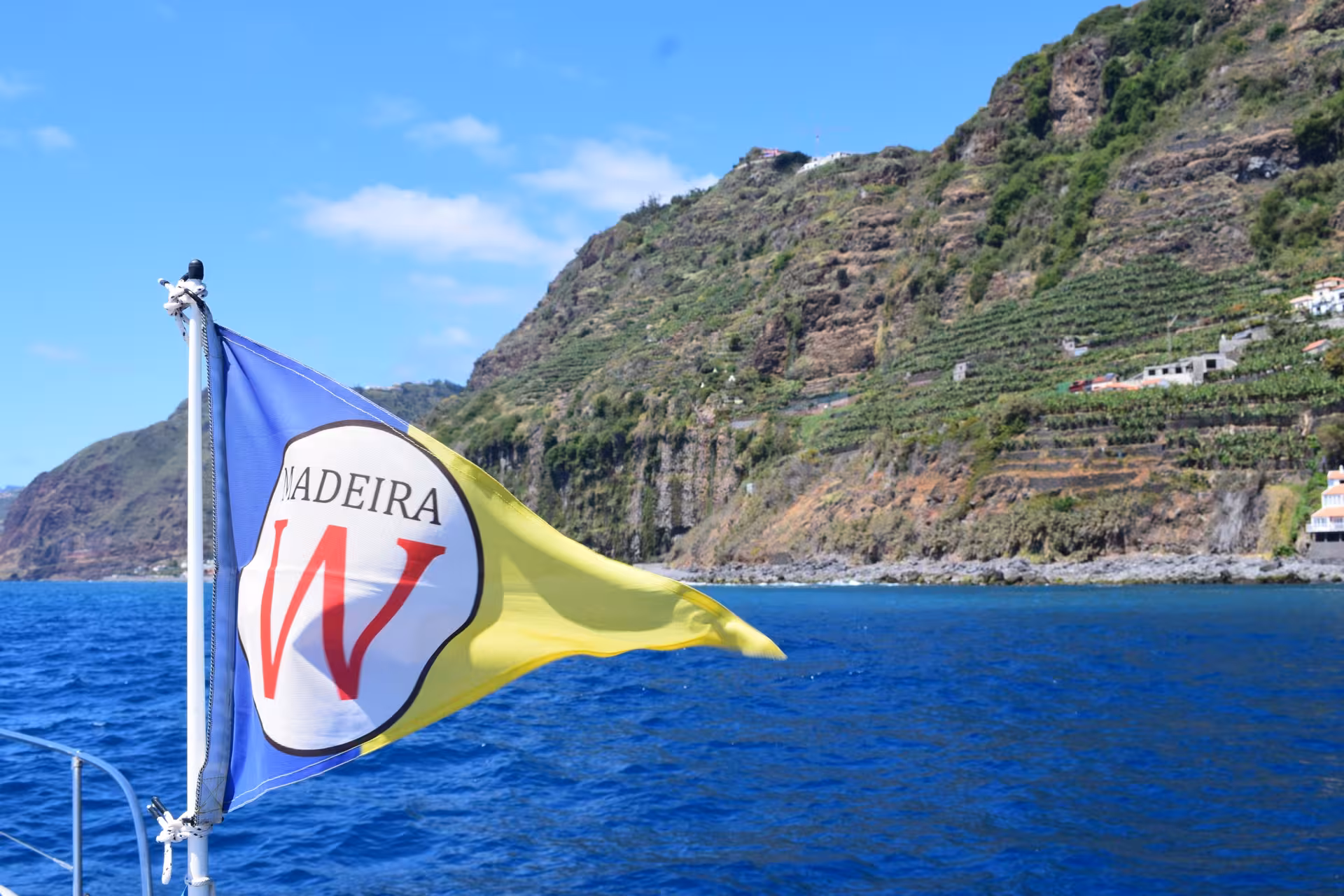 Madeira flag waving on a yacht with lush coastal cliffs in the background, ideal for GRINGO yacht half-day charters.