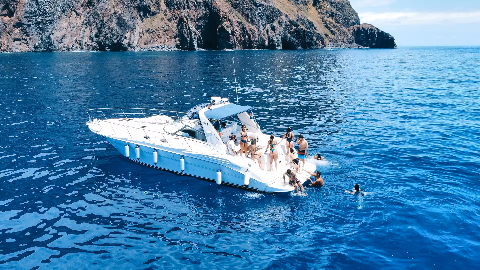 Group enjoying sunny day on GRINGO Yacht charter near rocky cliffs, perfect for private full-day adventures.