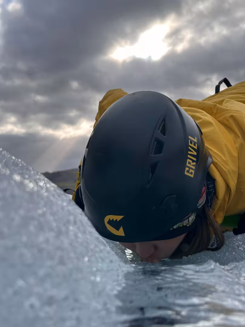 Hiker in yellow jacket and Grivel helmet lying on Solheimajokull glacier ice in Iceland