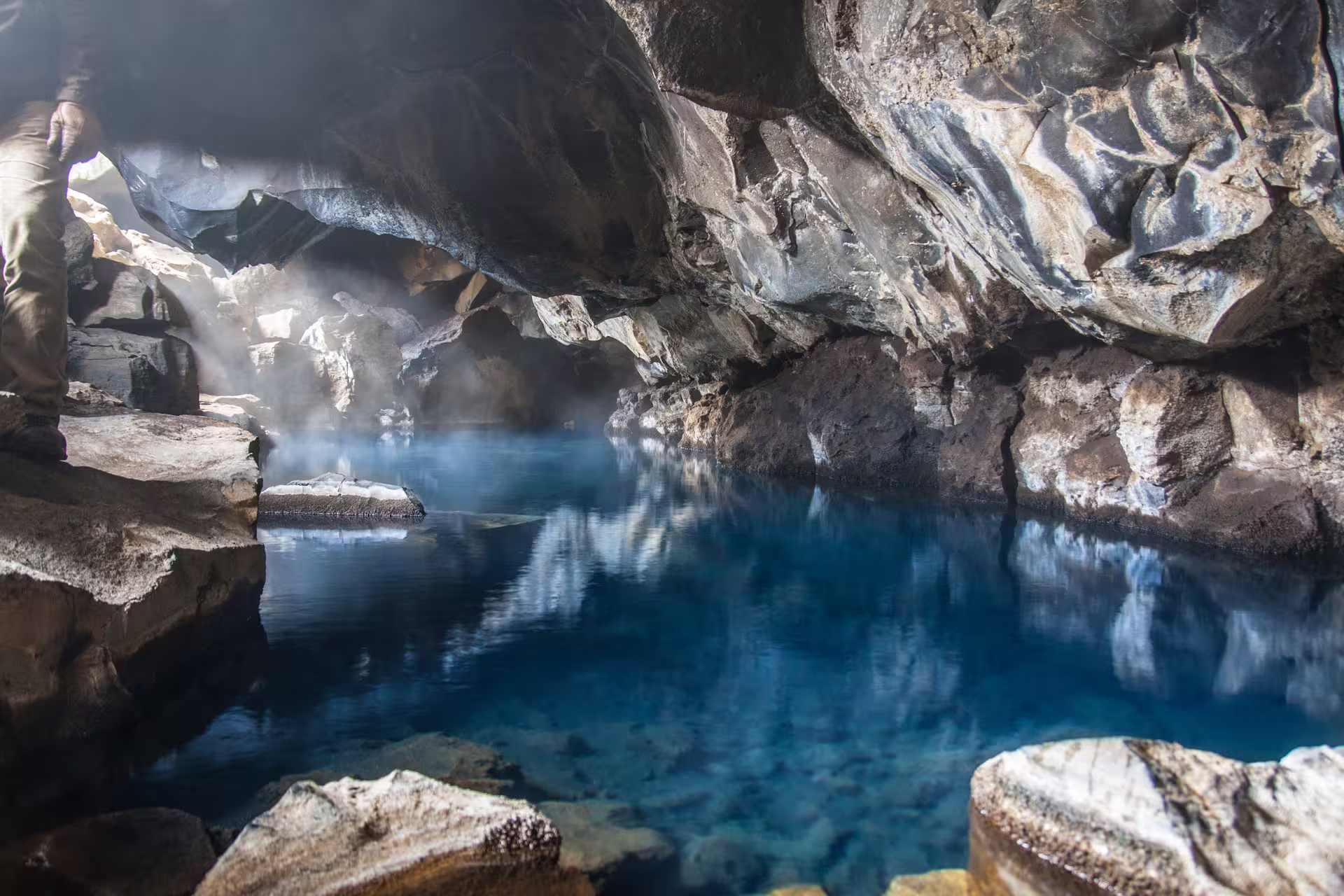 Steaming geothermal cave pool with vivid blue water and rocky walls in North Iceland