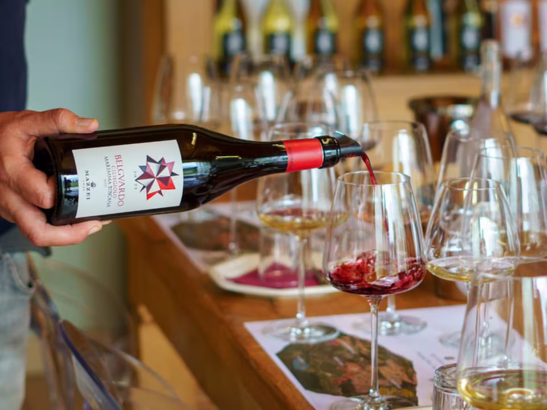 Pouring red wine into a glass during a tasting session at a Grosseto winery, showcasing a selection of six wines.
