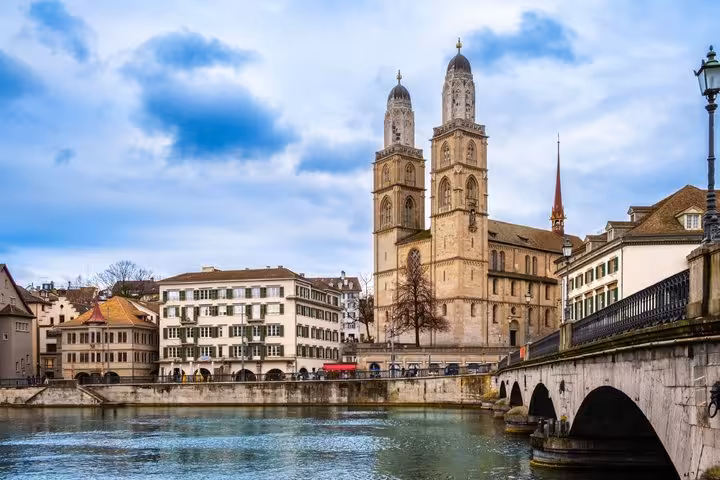 Grossmünster Cathedral twin towers rising above the Limmat River with stone bridge in Zurich old town