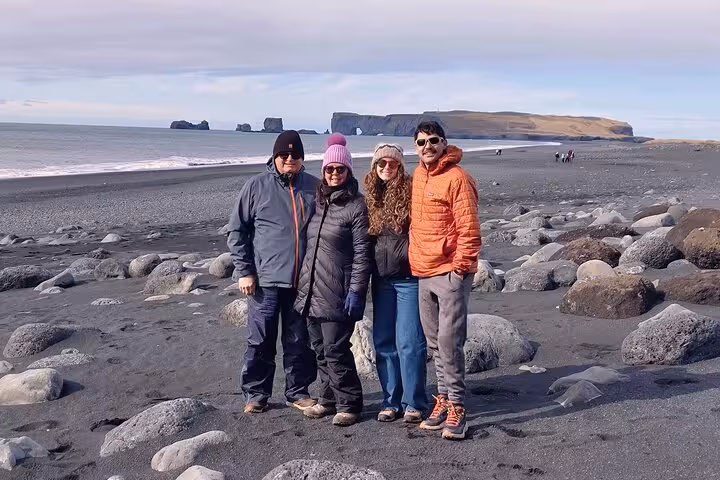 Four tourists posing on Reynisfjara black sand beach with dramatic sea stacks on Iceland's South Coast