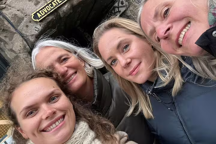 Four women smiling together on a gothic walking tour in Edinburgh's historic stone streets