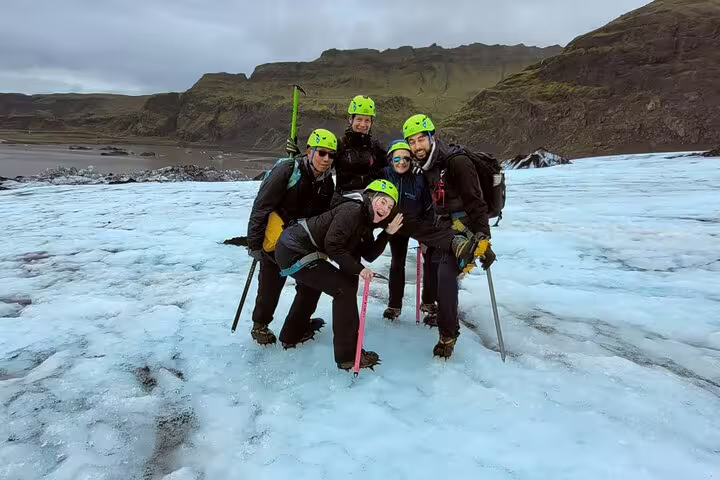 Four hikers in green helmets and crampons posing on Sólheimajökull glacier with ice axes