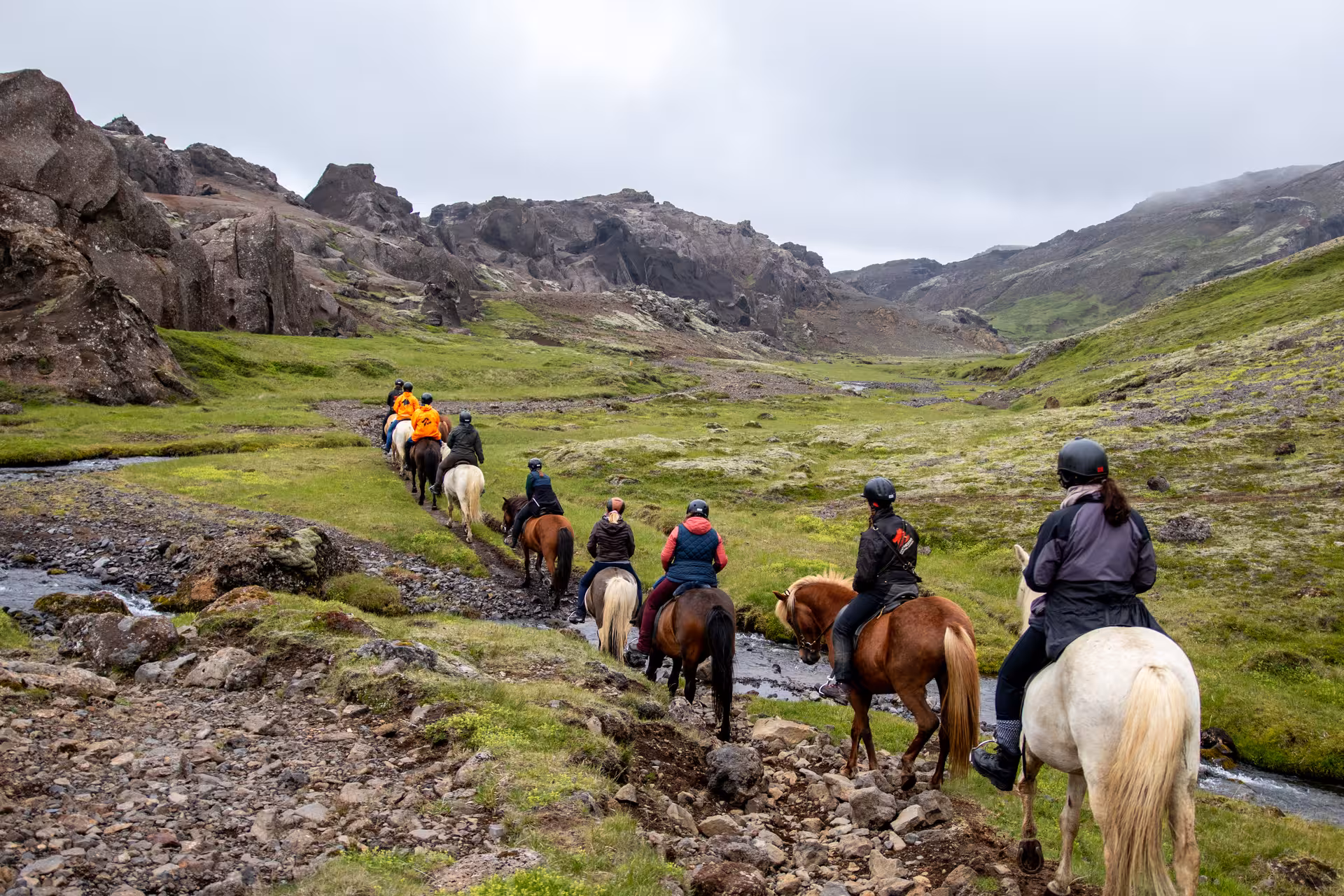 Group horseback riding through Marardalur Valley of Horses, Iceland, across green lava fields and streams
