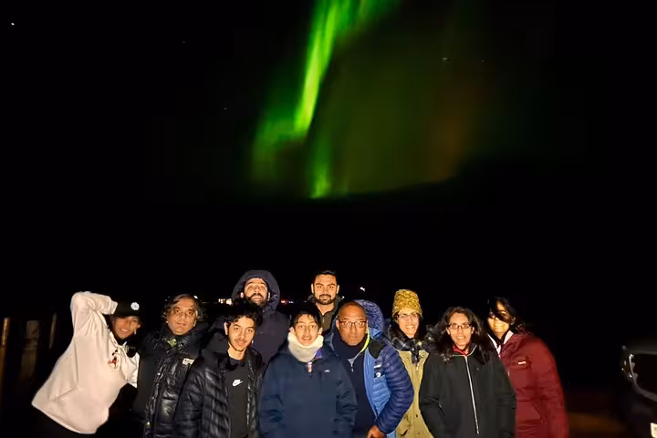 Group of tourists posing under vivid green northern lights in Reykjavik night sky