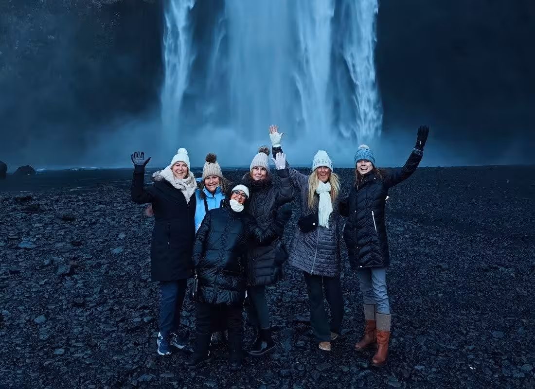 Group of six tourists waving in front of Skógafoss waterfall on Iceland South Coast tour