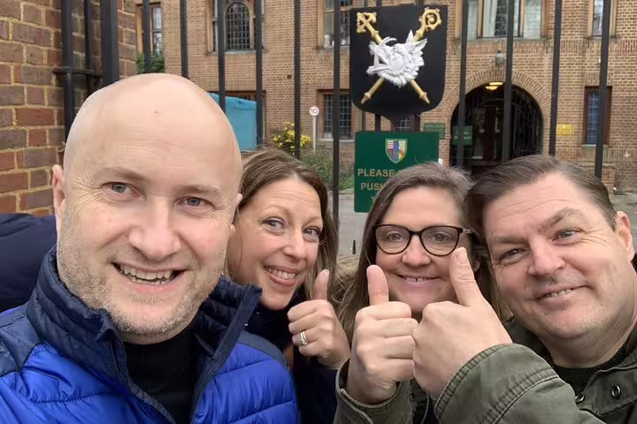 Four smiling tourists giving thumbs up outside historic Cambridge building on self-guided walking tour