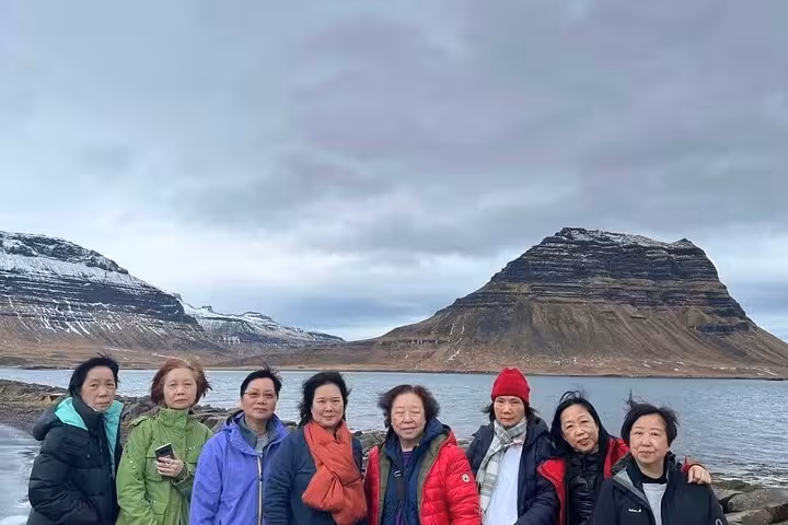Group of eight women posing by a fjord with snow-capped mountains in Snaefellsnes Peninsula, Iceland