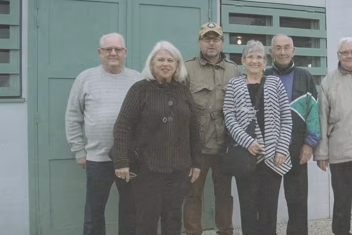 Group of six tourists posing together outside a green building during a D-Day Beaches tour in Normandy