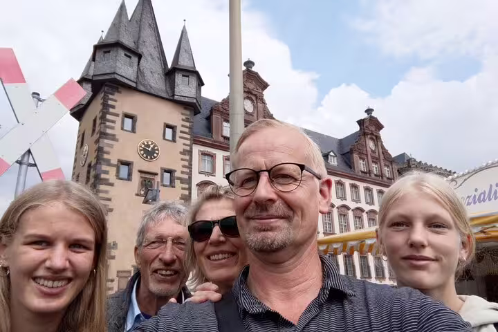 Group of five tourists smiling in selfie with Frankfurt Old Town historic clock tower behind them