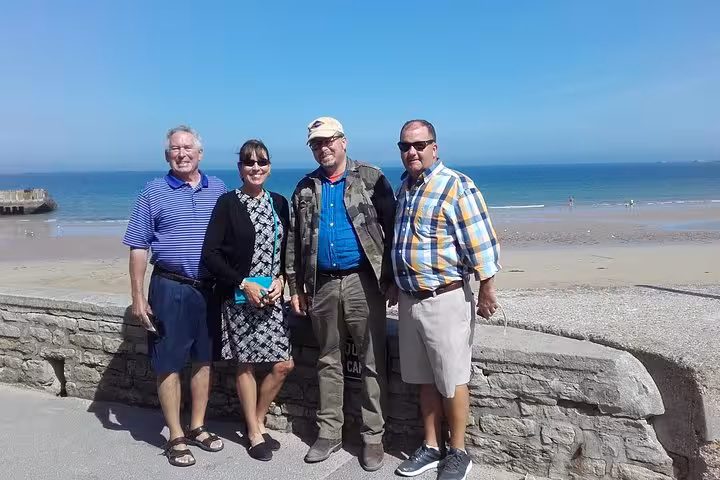 Four tourists posing together at Normandy beach seawall on D-Day Beaches private tour from Bayeux