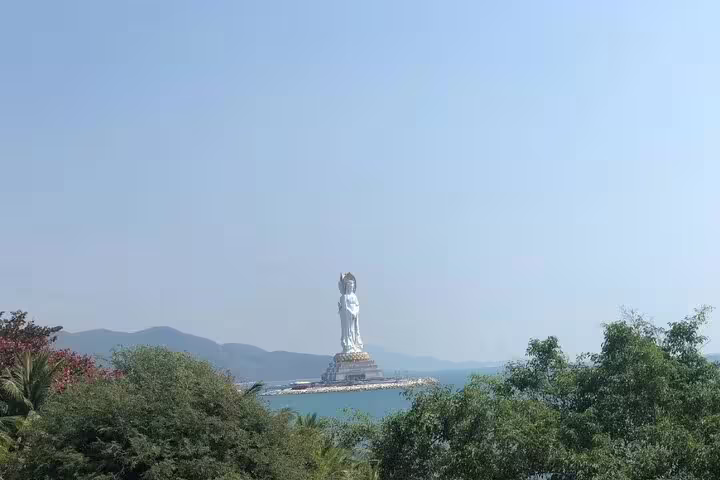 View of the majestic Guanyin statue at Nanshan Cultural Tourism Zone, Sanya, surrounded by lush greenery and ocean.