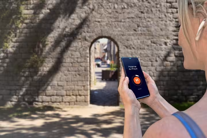 Woman using GPS audio guide app on smartphone at Poterne du Tricot stone arch gate in Guérande