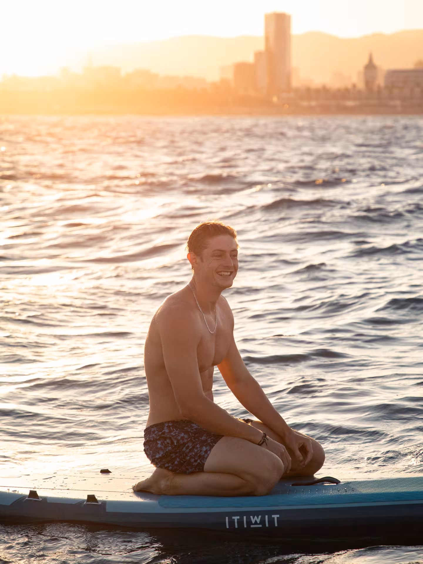 Guest kneeling on a paddleboard near the catamaran at sunset, enjoying an ocean adventure cruise