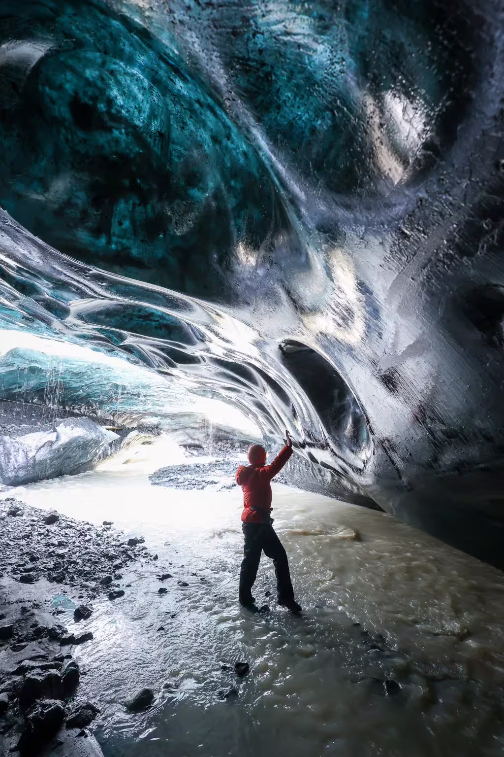 Tour guide in red jacket touching stunning blue glacial ice walls inside an Iceland sapphire ice cave adventure