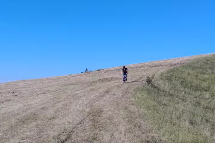 Cyclist riding uphill on a grassy trail in Transylvania countryside under clear blue sky