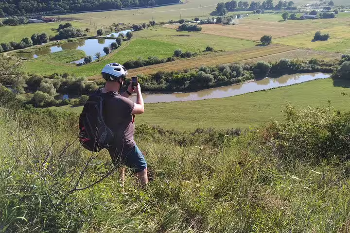 Cyclist in helmet photographing scenic Transylvania river valley and farmland from hilltop viewpoint