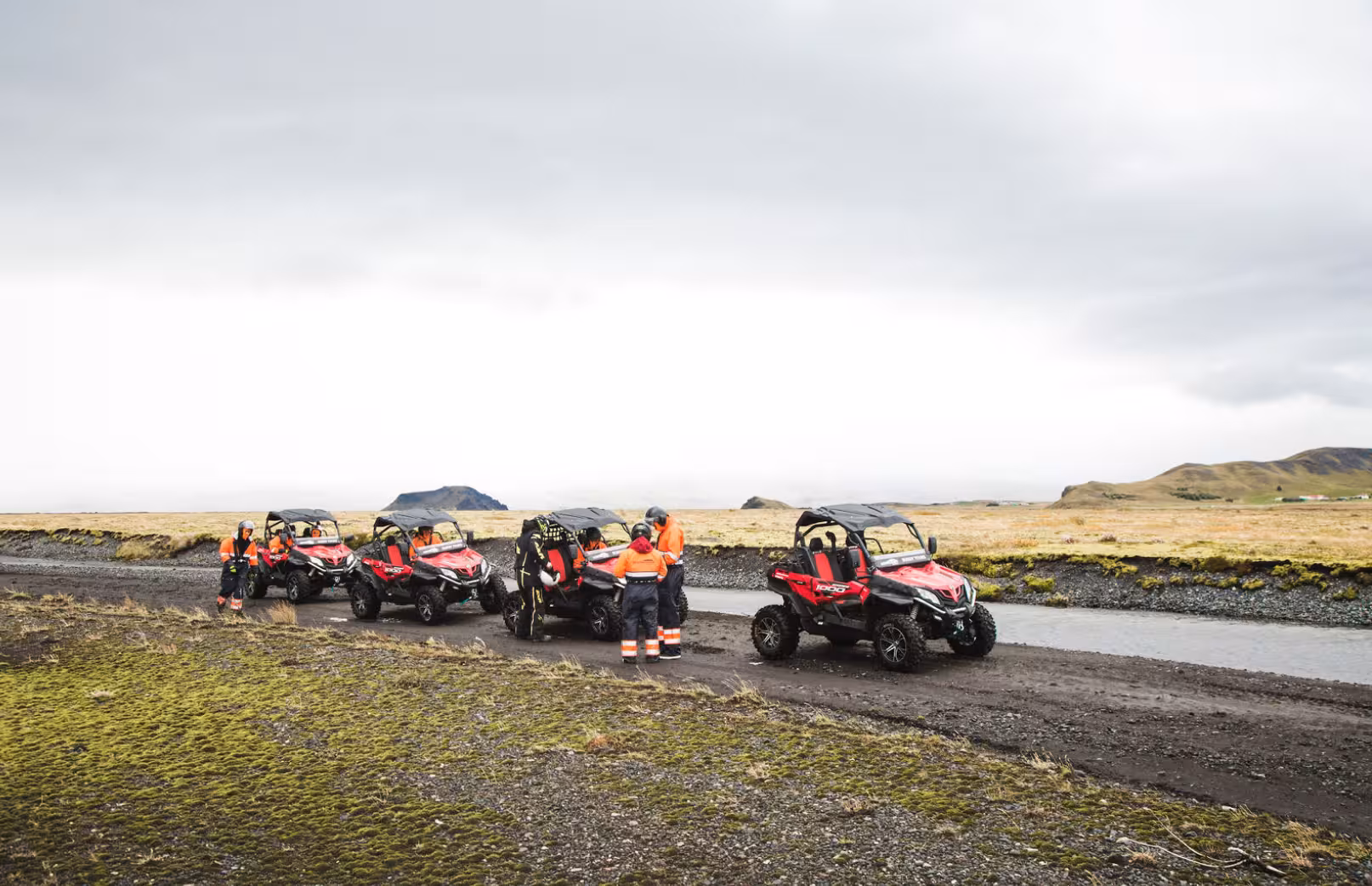 Group of red buggies with guides in orange safety gear on a gravel track in Iceland's volcanic landscape