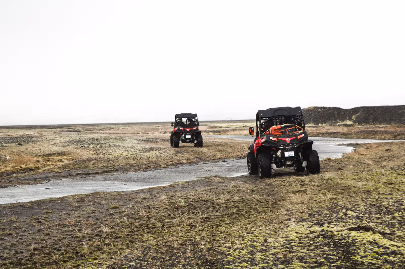 Two red and black buggy UTVs driving through rugged Icelandic lava field terrain on a guided tour
