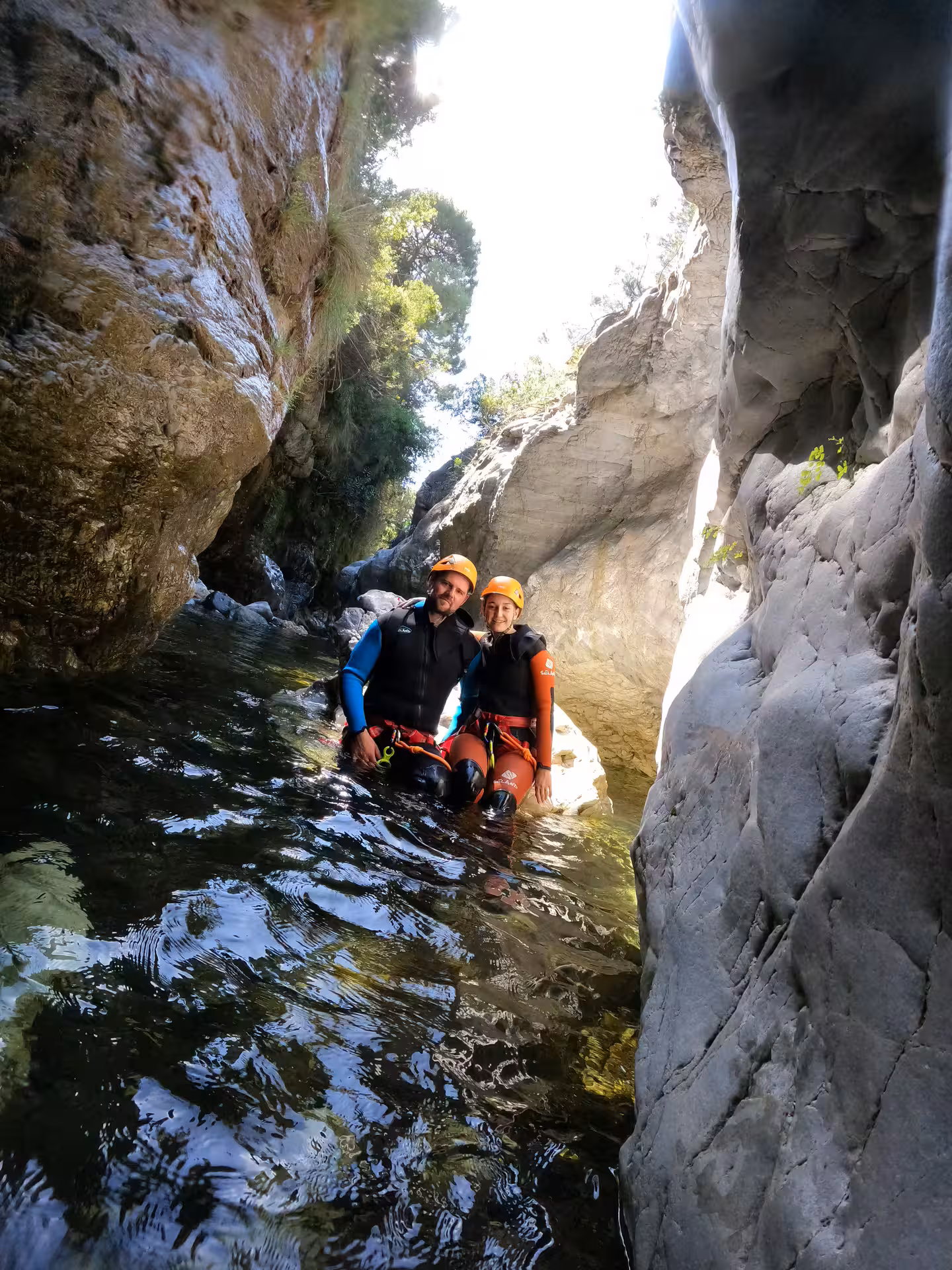 Couple in wetsuits and helmets wading through narrow canyon slot on guided canyoning tour Guadalmina Canyon Estepona
